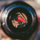 De lens van een camera is vol in beeld. Het beeld zelf is geblurd. Er is in het midden van de lens een foto te zien van een rode auto op zijn kop